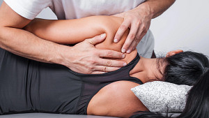 Posterior view of a masseuse massaging a woman&#039;s upper shoulder.