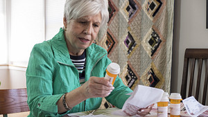 Woman sitting at a table reading the label on a prescription bottle