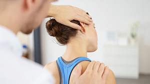 Male physical therapist massaging a young woman&#039;s neck in the medical office